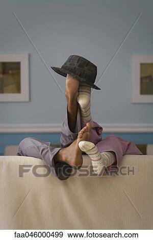Two people reclining on sofa, legs raised together, hat set atop feet, rear view View Large Photo Image Stock Photo - Two people reclining on sofa, legs raised together, hat set atop feet, rear view. Fotosearch