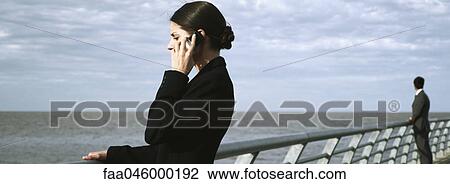 Stock Image - Woman at waterfront railing using cell phone. Fotosearch