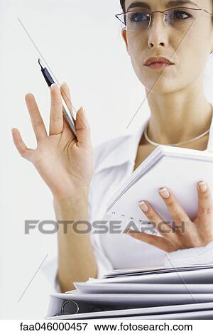Woman holding notepad, looking away in thought, stack of binders in foreground View Large Photo Image Stock Photo - Woman holding notepad, looking away in thought, stack of binders in foreground. Fotosearch