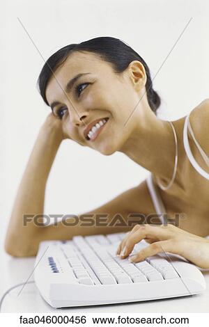 Woman leaning on elbow typing on keyboard, smiling View Large Photo Image Stock Photograph - Woman leaning on elbow typing on keyboard, smiling. Fotosearch