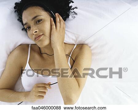 Woman lying on bed listening to headphones View Large Photo Image Stock Photo - Woman lying on bed listening to headphones. Fotosearch