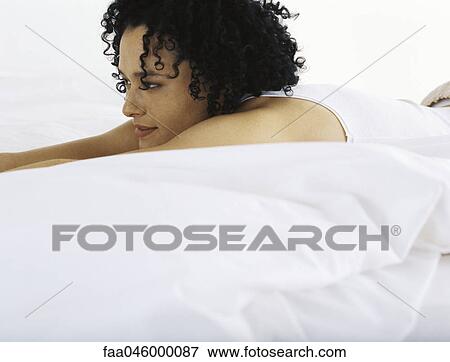 Stock Photo - Woman lying on bed, looking away in thought. Fotosearch
