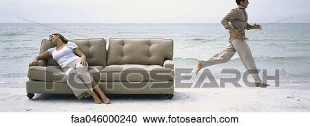 Woman napping on sofa on beach, man running past in background View Large Photo Image Stock Image - Woman napping on sofa on beach, man running past in background. Fotosearch