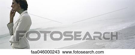 Stock Image - Woman on beach using cell phone, admiring view. Fotosearch