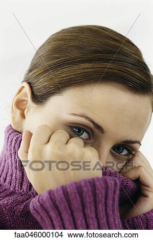 Picture - Woman pulling turtleneck collar over mouth and nose, portrait. Fotosearch