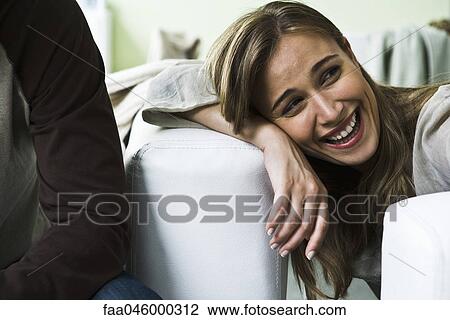 Stock Image - Woman resting head on arm, looking away laughing. Fotosearch