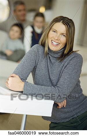 Woman sitting on floor smiling at camera, family on sofa in background View Large Photo Image Stock Photo - Woman sitting on floor smiling at camera, family on sofa in background. Fotosearch