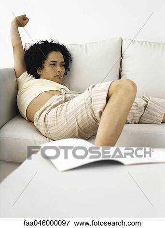 Stock Photo - Woman sitting on sofa stretching. Fotosearch