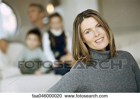 Woman smiling at camera, family on sofa in background View Large Photo Image Stock Image - Woman smiling at camera, family on sofa in background. Fotosearch