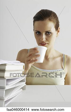 Woman taking break, drinking from disposable cup, stack of binders in foreground View Large Photo Image Picture - Woman taking break, drinking from disposable cup, stack of binders in foreground. Fotosearch
