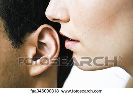 Stock Photo - Woman whispering in man's ear, close-up. Fotosearch