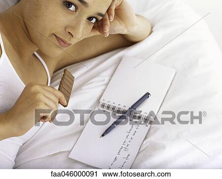 Young woman eating chocolate and writing in diary View Large Photo Image Stock Image - Young woman eating chocolate and writing in diary. Fotosearch