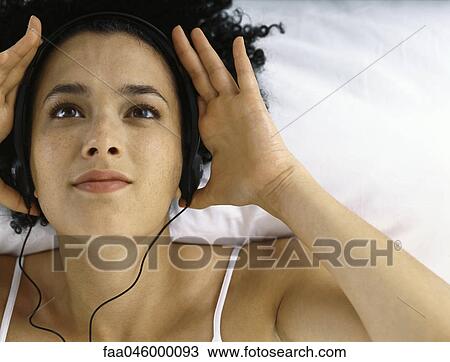Young woman lying on back listening to headphones View Large Photo Image Stock Image - Young woman lying on back listening to headphones. Fotosearch