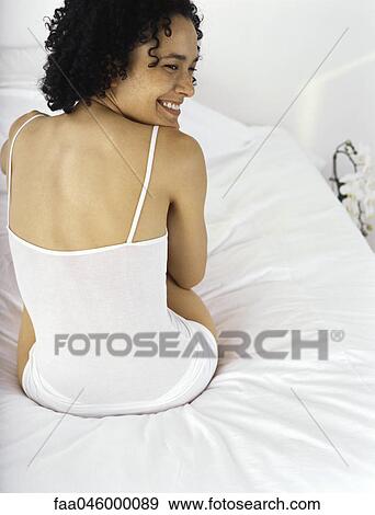 Young woman sitting on bed in underwear, looking away smiling View Large Photo Image Stock Photo - Young woman sitting on bed in underwear, looking away smiling. Fotosearch