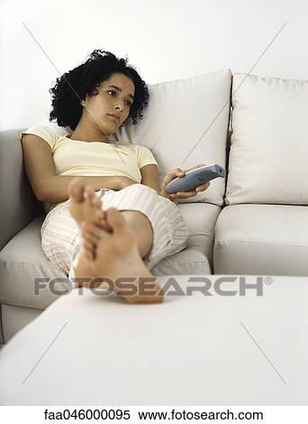 Young woman sitting on sofa idly changing channels View Large Photo Image Stock Photography - Young woman sitting on sofa idly changing channels. Fotosearch