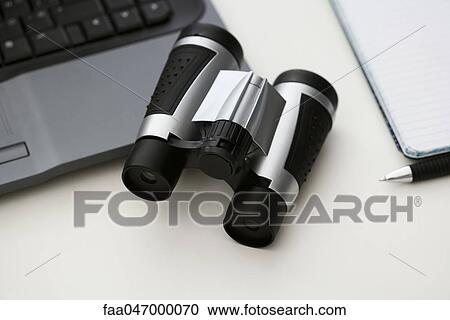 Stock Image - Binoculars on desk with laptop computer and notebook. Fotosearch
