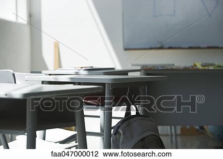 Stock Image - Bookbag hanging from desk in empty classroom. Fotosearch