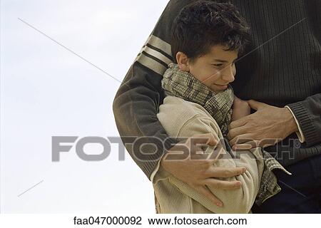 Stock Image - Boy being embraced by father, cropped. Fotosearch