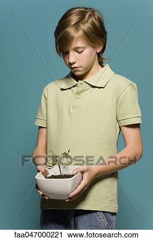 Stock Image - Boy holding wilted potted plant. Fotosearch