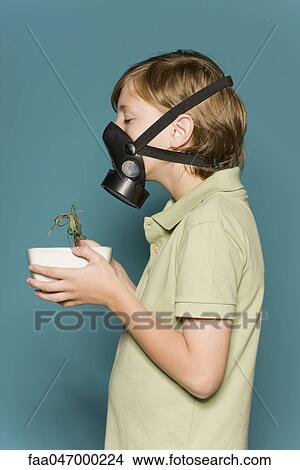 Picture - Boy wearing gas mask, holding wilted potted plant. Fotosearch