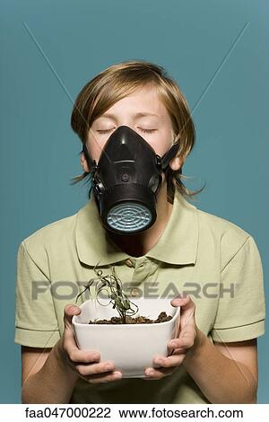 Stock Image - Boy wearing gas mask, holding wilted potted plant. Fotosearch