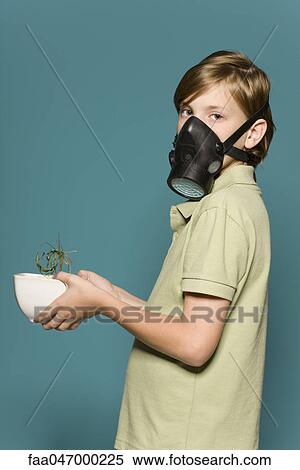 Stock Photography - Boy wearing gas mask, holding wilted potted plant. Fotosearch