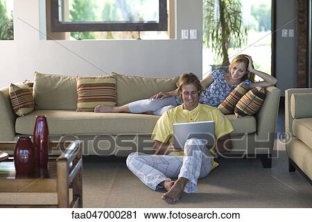 Couple together in living room, woman reclining on sofa, man sitting on floor with laptop computer View Large Photo Image Stock Image - Couple together in living room, woman reclining on sofa, man sitting on floor with laptop computer. Fotosearch