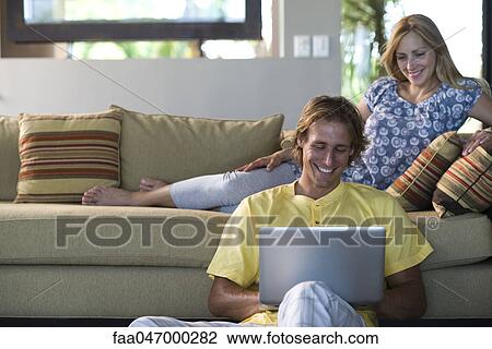 Couple together in living room, woman reclining on sofa, man sitting on floor with laptop computer View Large Photo Image Stock Image - Couple together in living room, woman reclining on sofa, man sitting on floor with laptop computer. Fotosearch