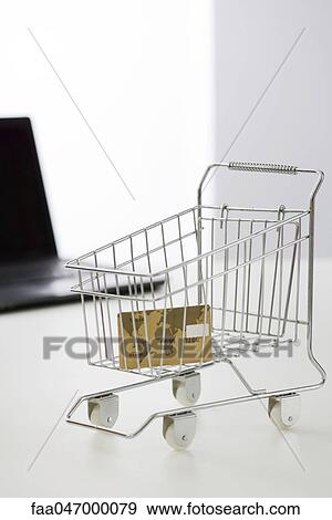Stock Photo - Credit card in miniature shopping cart, laptop computer in background. Fotosearch