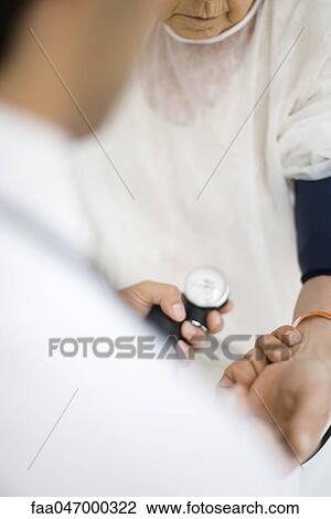 Stock Image - Doctor checking patient's blood pressure, over shoulder view. Fotosearch