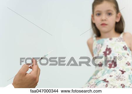 Doctor holding syringe, preparing to vaccinate little girl, cropped View Large Photo Image Picture - Doctor holding syringe, preparing to vaccinate little girl, cropped. Fotosearch