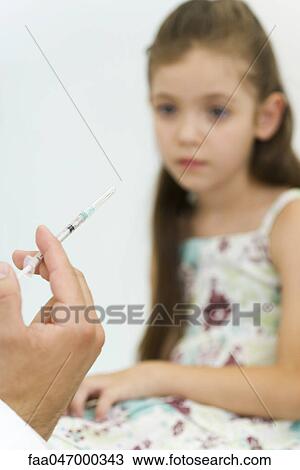 Stock Image - Doctor holding syringe, preparing to vaccinate little girl, cropped. Fotosearch