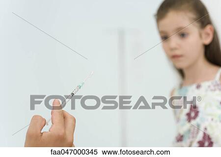Stock Photography - Doctor holding syringe, preparing to vaccinate little girl, cropped. Fotosearch