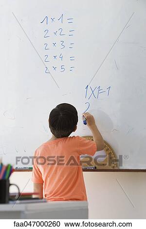 Stock Image - Elementary school student doing math equation on whiteboard, rear view. Fotosearch
