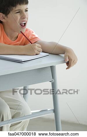 Stock Photo - Elementary school student taking notes in classroom, squinting at board. Fotosearch