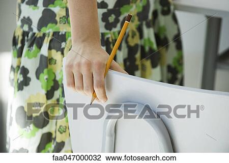 Stock Image - Female standing beside chair, pencil in hand, cropped. Fotosearch