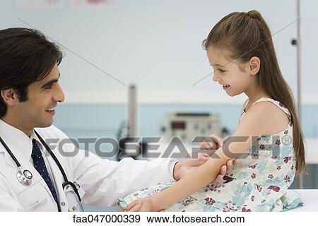 Friendly doctor examining little girl's arm View Large Photo Image Stock Photo - Friendly doctor examining little girl's arm. Fotosearch
