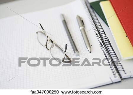 Stock Image - Glasses, pens on open notebook. Fotosearch