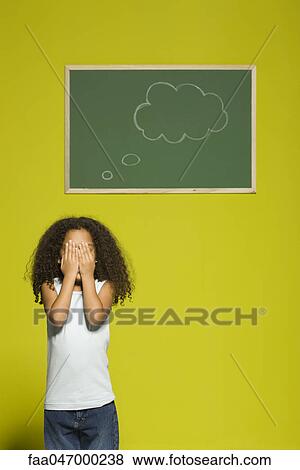 Stock Photo - Little girl covering eyes with hands, thought bubble on chalkboard behind her. Fotosearch