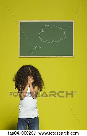 Stock Photo - Little girl covering face with hands, thought bubble on chalkboard behind her. Fotosearch