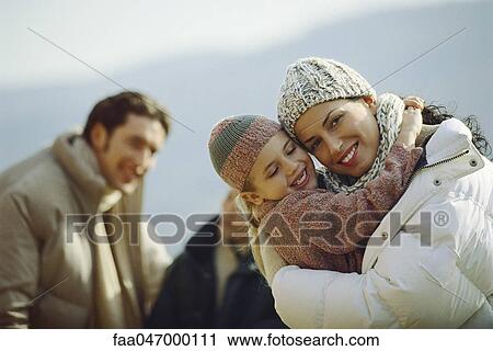 Little girl embracing mother, family in background View Large Photo Image Stock Image - Little girl embracing mother, family in background. Fotosearch