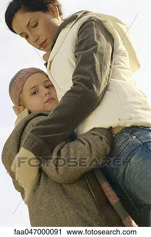 Stock Image - Little girl embracing mother, low angle view. Fotosearch
