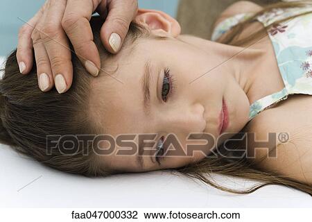 Stock Image - Little girl lying on back, parent stroking her forehead, cropped. Fotosearch