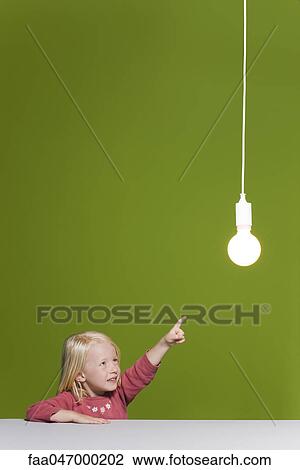Stock Image - Little girl pointing at illuminated light bulb suspended overhead. Fotosearch