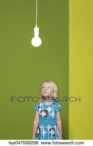 Stock Photograph - Little girl staring up at illuminated light bulb suspended overhead. Fotosearch