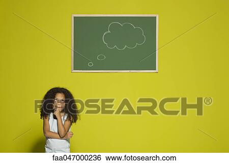 Stock Photograph - Little girl thinking, empty thought bubble on chalkboard overhead. Fotosearch