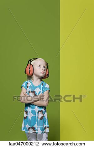 Stock Image - Little girl with arms folded, wearing protective headphones, defiantly looking away. Fotosearch