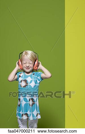 Stock Image - Little girl with eyes closed wearing protective headphones. Fotosearch