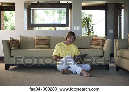 Stock Image - Man sitting on living room floor using laptop computer. Fotosearch