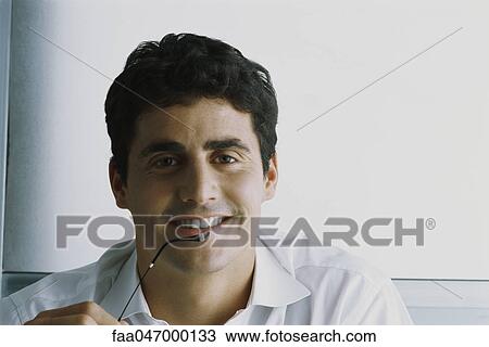 Stock Image - Man smiling at camera, holding glasses, portrait. Fotosearch